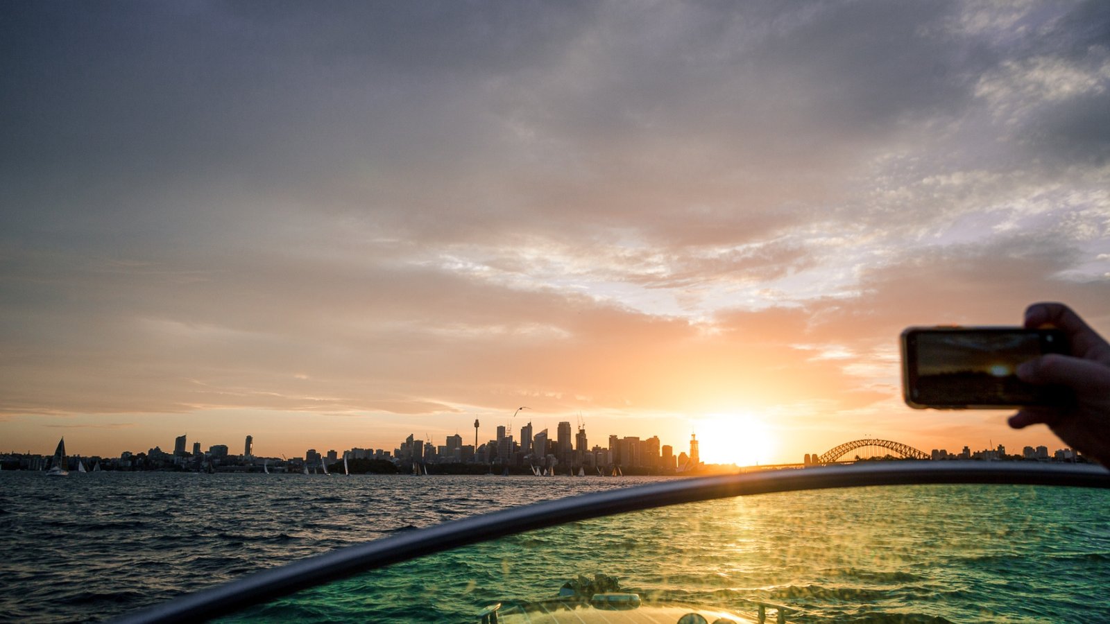 Sunset over Sydney Harbour with city skyline and Sydney Harbour Bridge visible, taken from a boat.