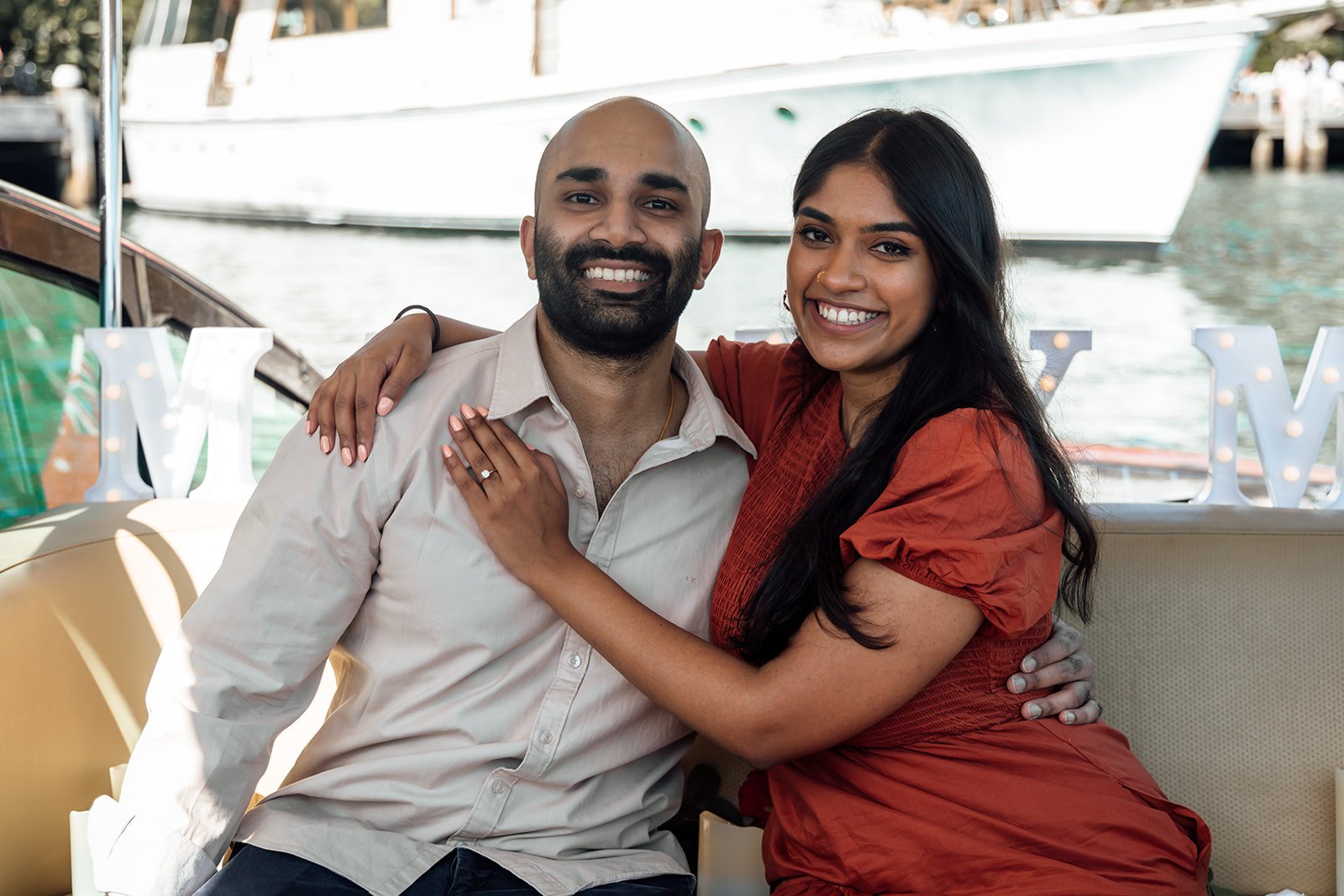 Woman showing engagement ring on yacht decorated with a marry me sign