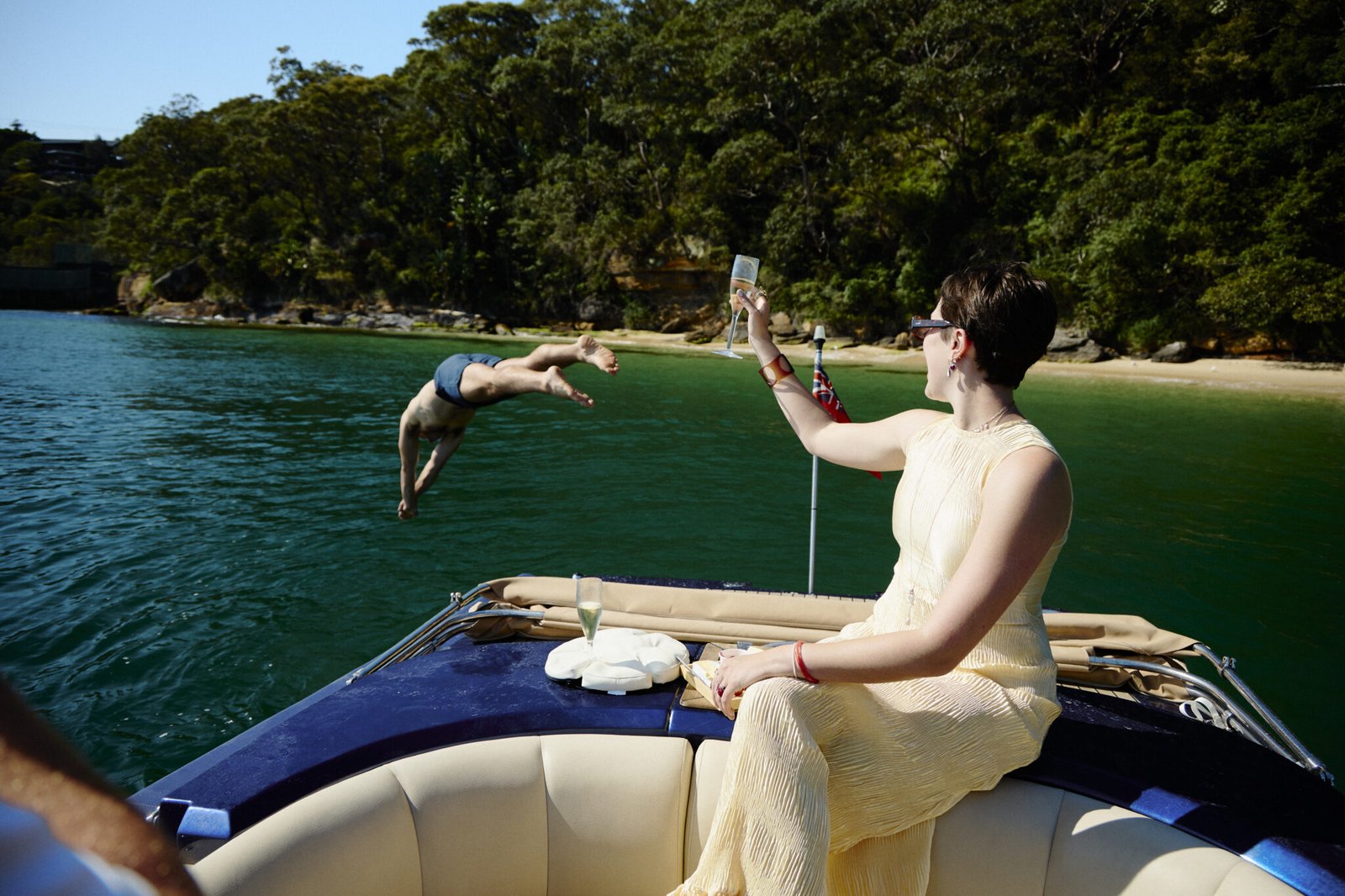 Woman raising champagne glass as man dives off MV Aquamajestic into Sydney Harbour.