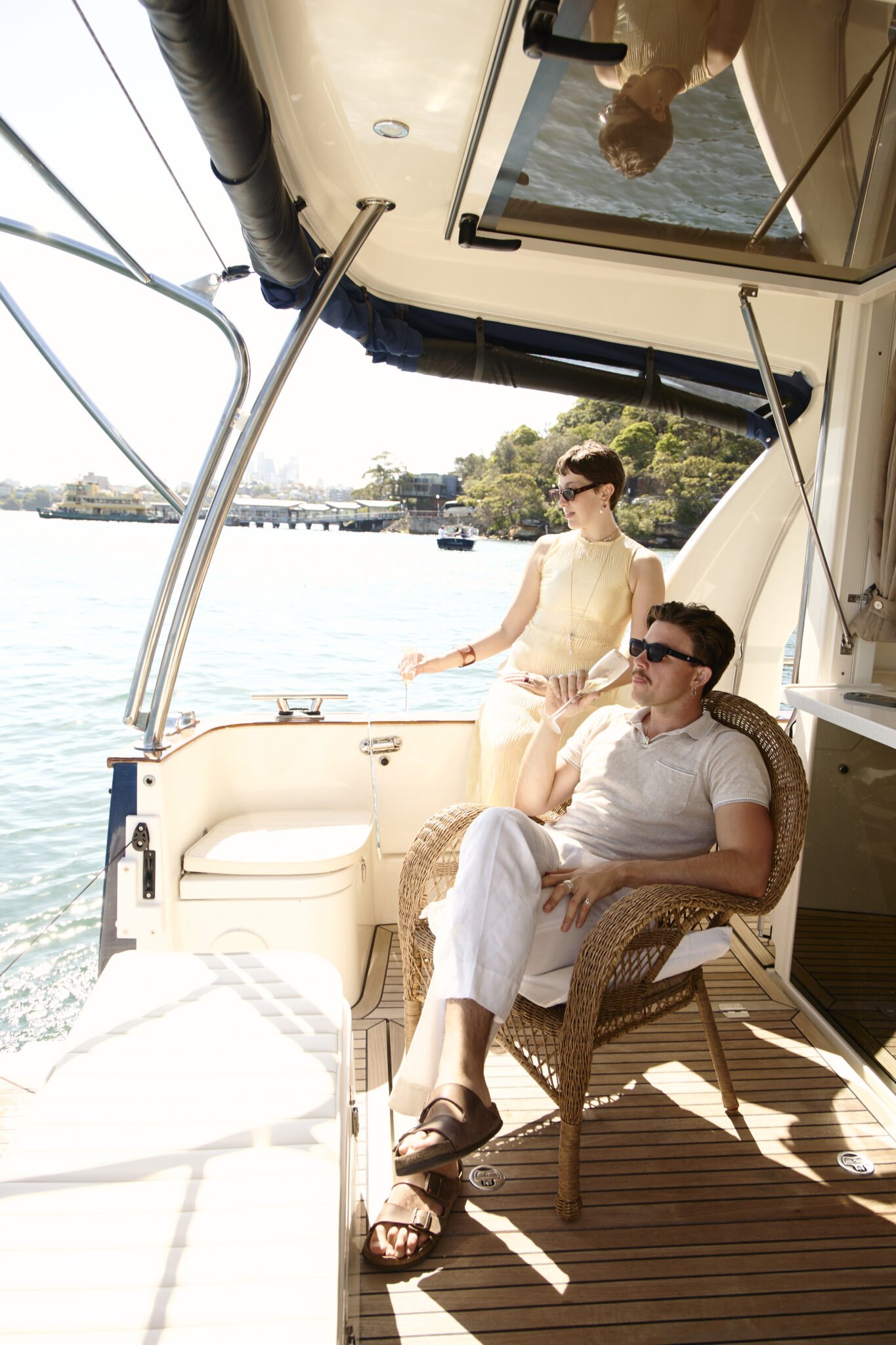 Couple relaxing in the shaded rear deck lounge of EV Arcadia electric charter yacht on Sydney Harbour.