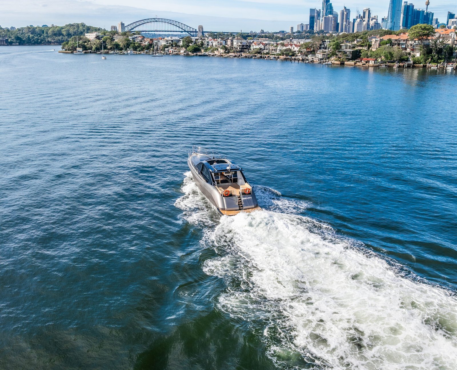 MV Gravity speeding through harbour with city skyline in distance.